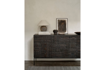 Dark carved wooden sideboard with three doors styled with ceramic decor, framed artwork, and a table lamp in a modern neutral interior.