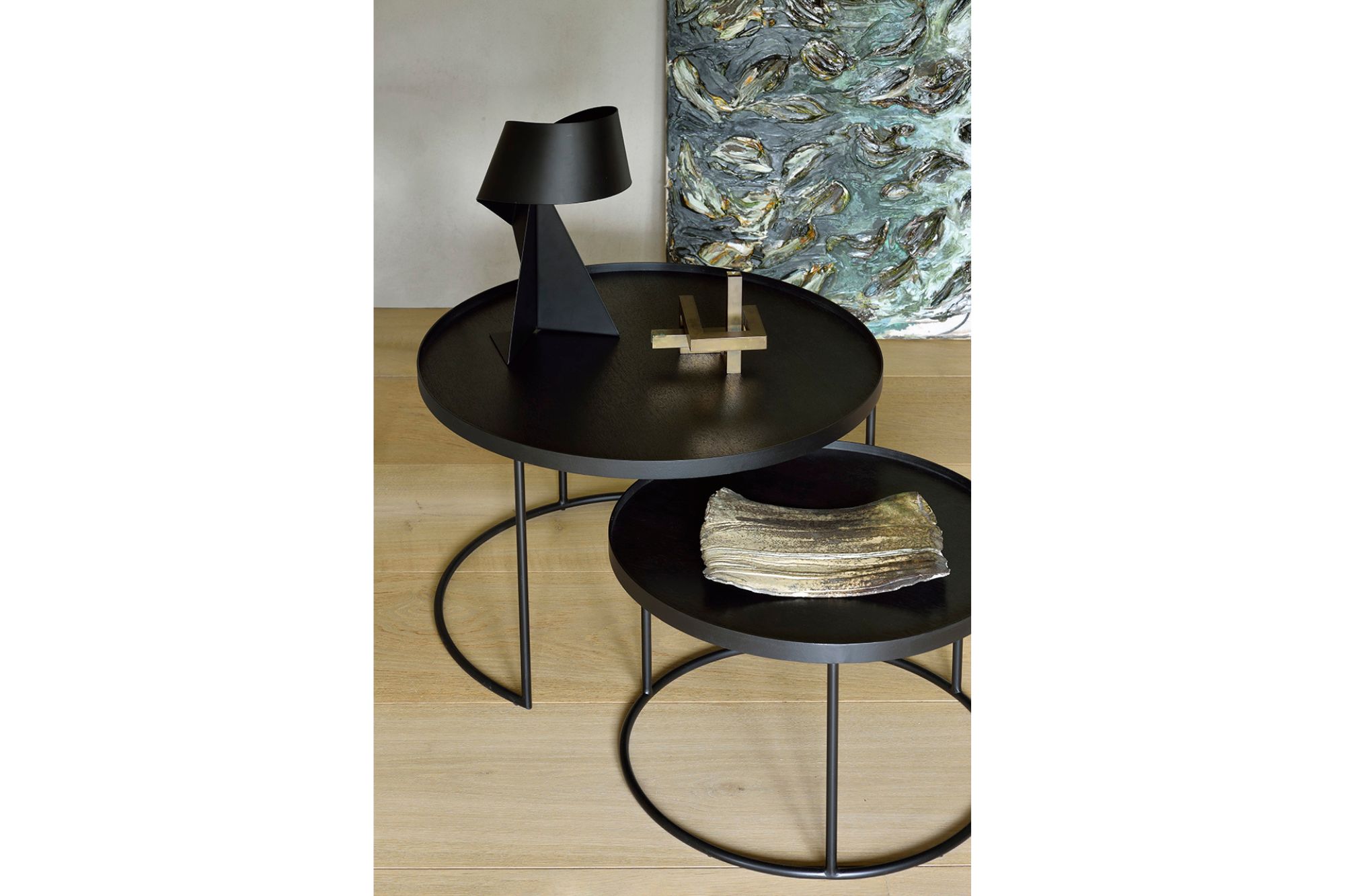 Modern black nesting coffee tables with slim metal frames, styled with sculptural decor and placed on light wood flooring next to abstract wall art.