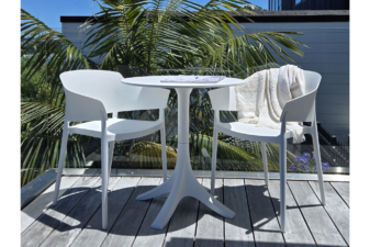 Modern white outdoor bistro set with two armchairs and a round pedestal table on a wooden deck, surrounded by lush tropical greenery under a clear blue sky.