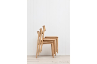Side view of three stackable light oak dining chairs with tan leather seats, showcasing space-saving design and clean Scandinavian lines against a white paneled wall.