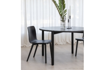 Modern black wooden dining tables nz featuring a round wooden table and curved chairs, styled with minimalist decor including a ribbed glass vase and taper candles, set in a bright space with sheer curtains. cuchi nz
