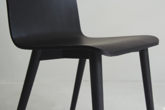 Close-up of a black wooden dining chair highlighting its smooth curved seat and tapered leg design, crafted in a sleek, minimalist style.